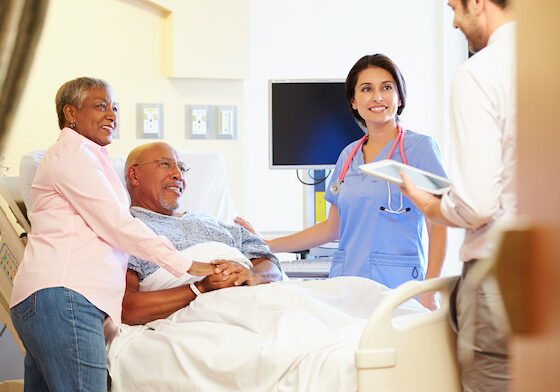 Medical Team Meeting With Senior Couple In Hospital Room